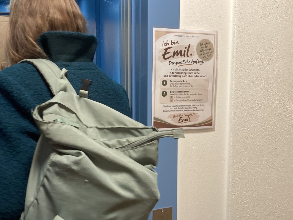 Plakat „Ich bin Emil. Der gemütliche Aufzug“ neben der Aufzugtür im Dorfcafé Gleiritsch