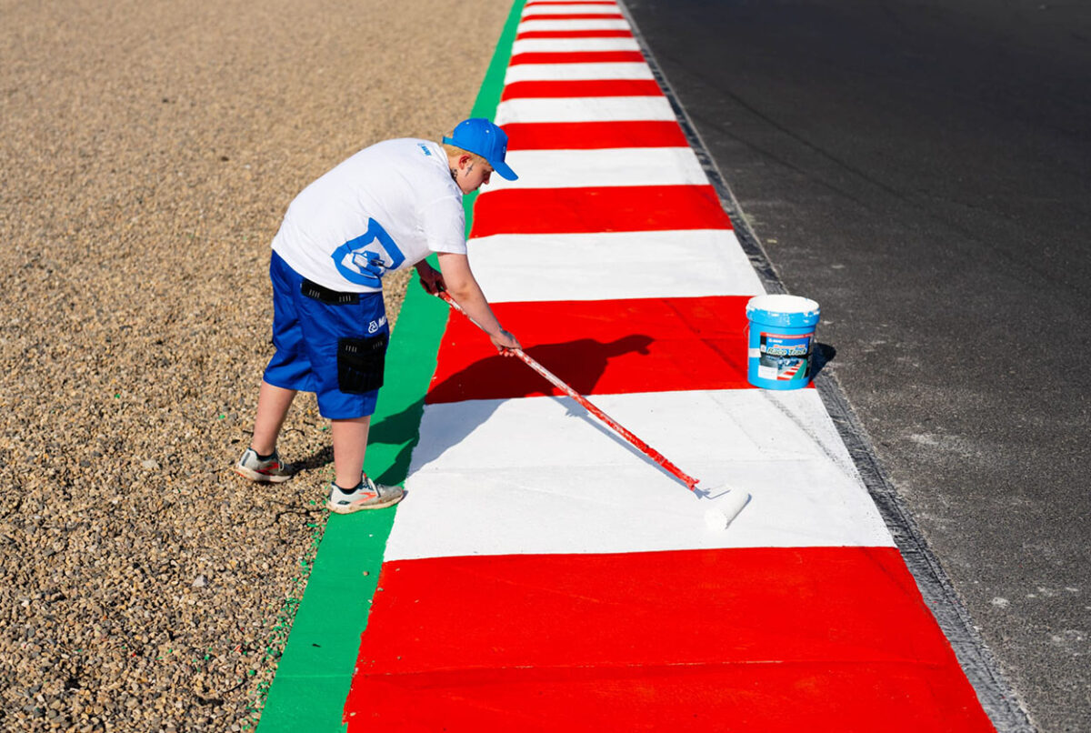 Ein Arbeiter beschichtet rot-weiße Randsteine am Autodrom Most